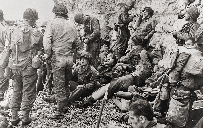 First Infantry assault troops who made it to the chalk cliffs take a breather before moving inland, shielded from danger for the moment. Meanwhile, medics who landed with the men attend to the injured.